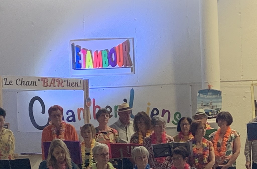 Les Chants'berlières en costumes colorés lors du Spectacle Fantaisie devant un panneau « Le Tambour »